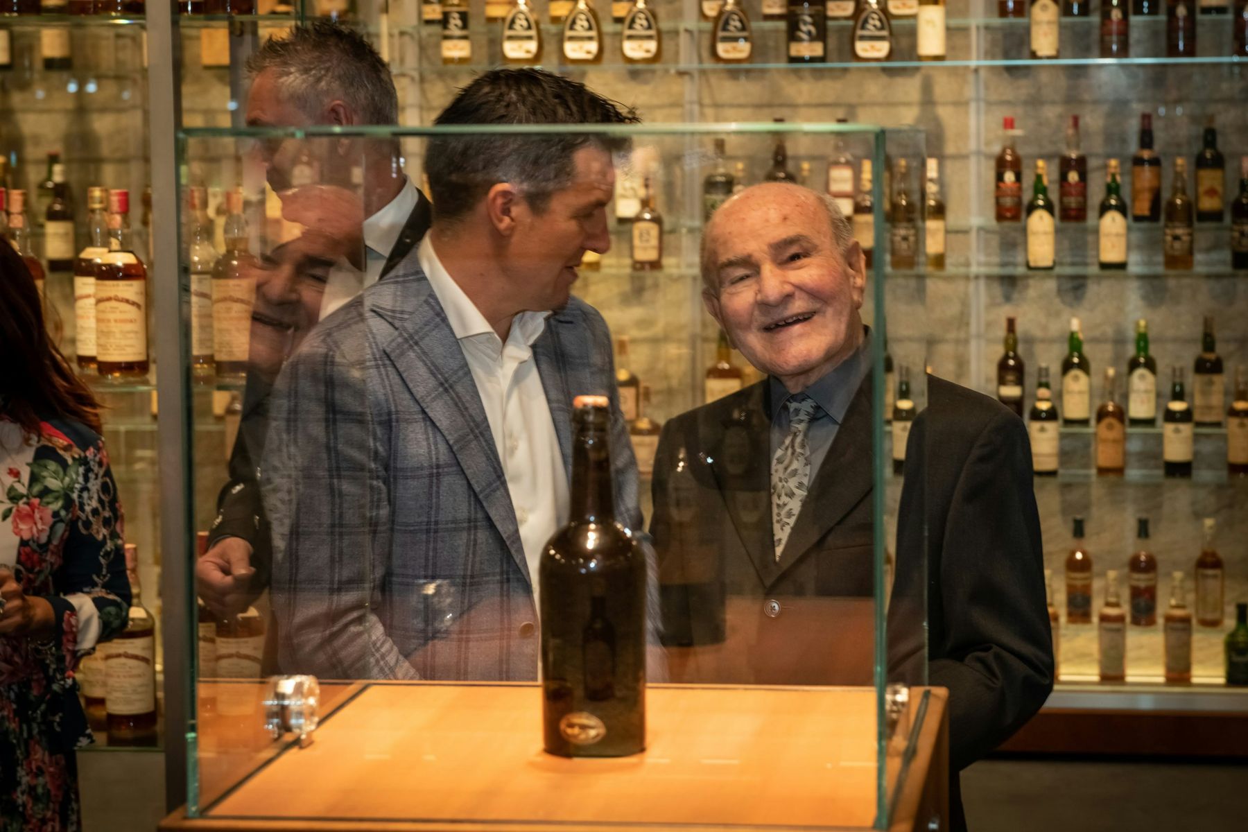 Valentino Zagatti smiling beside the 1843 bottle in its glass case at the opening